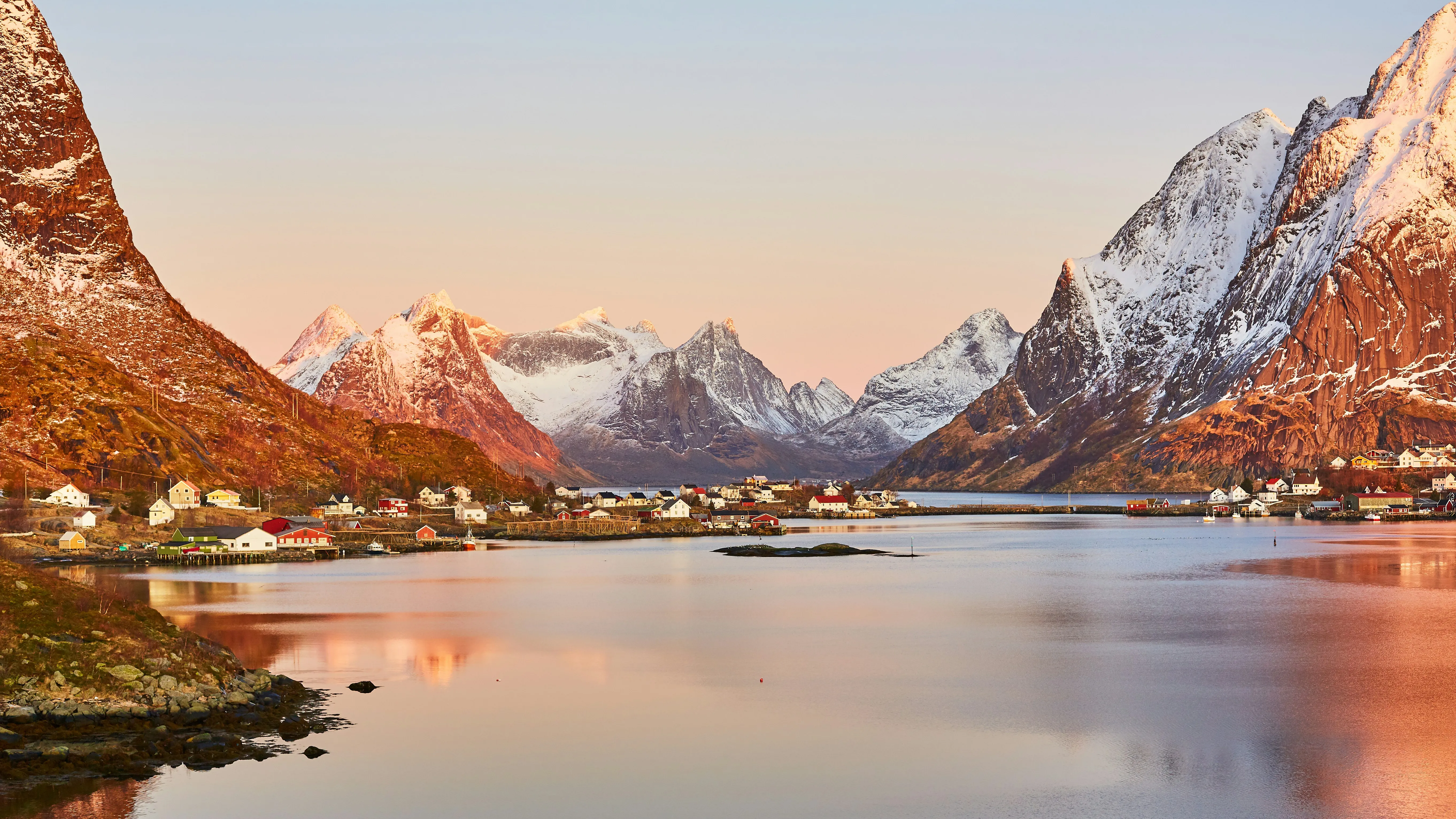 Norwegian fjord village surrounded by snow-capped mountains at sunset