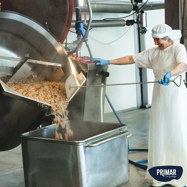 A worker in the Primar factory tilting a large industrial cooking pot, pouring freshly made bacalao into a steel container