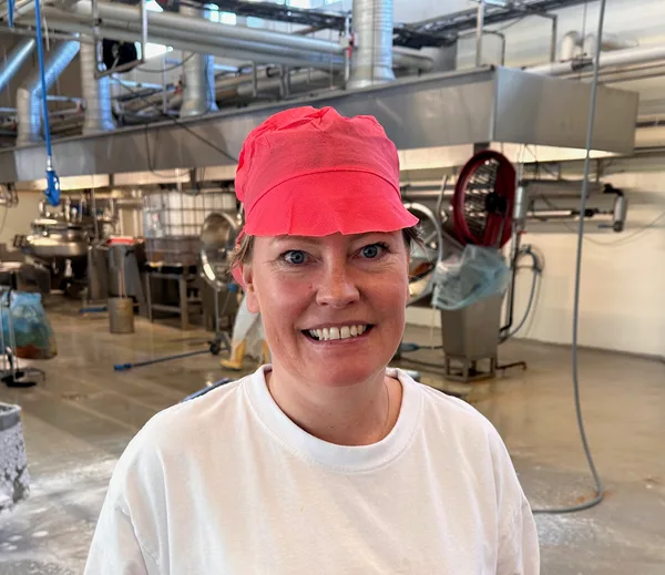 Sissel Opshaug smiling at the camera in the Primar bacalao factory, wearing a white t-shirt and red factory cap