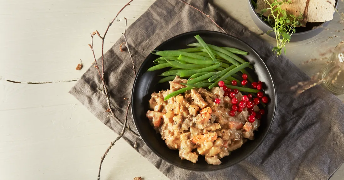 A bowl of Primar's wild game stew with green beans and lingonberries, served on a rustic table setting