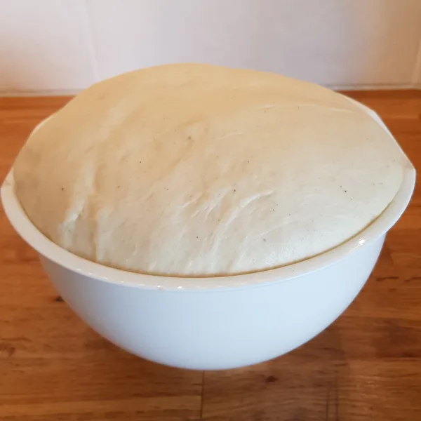 Perfectly risen cinnamon bun dough overflowing from a white mixing bowl