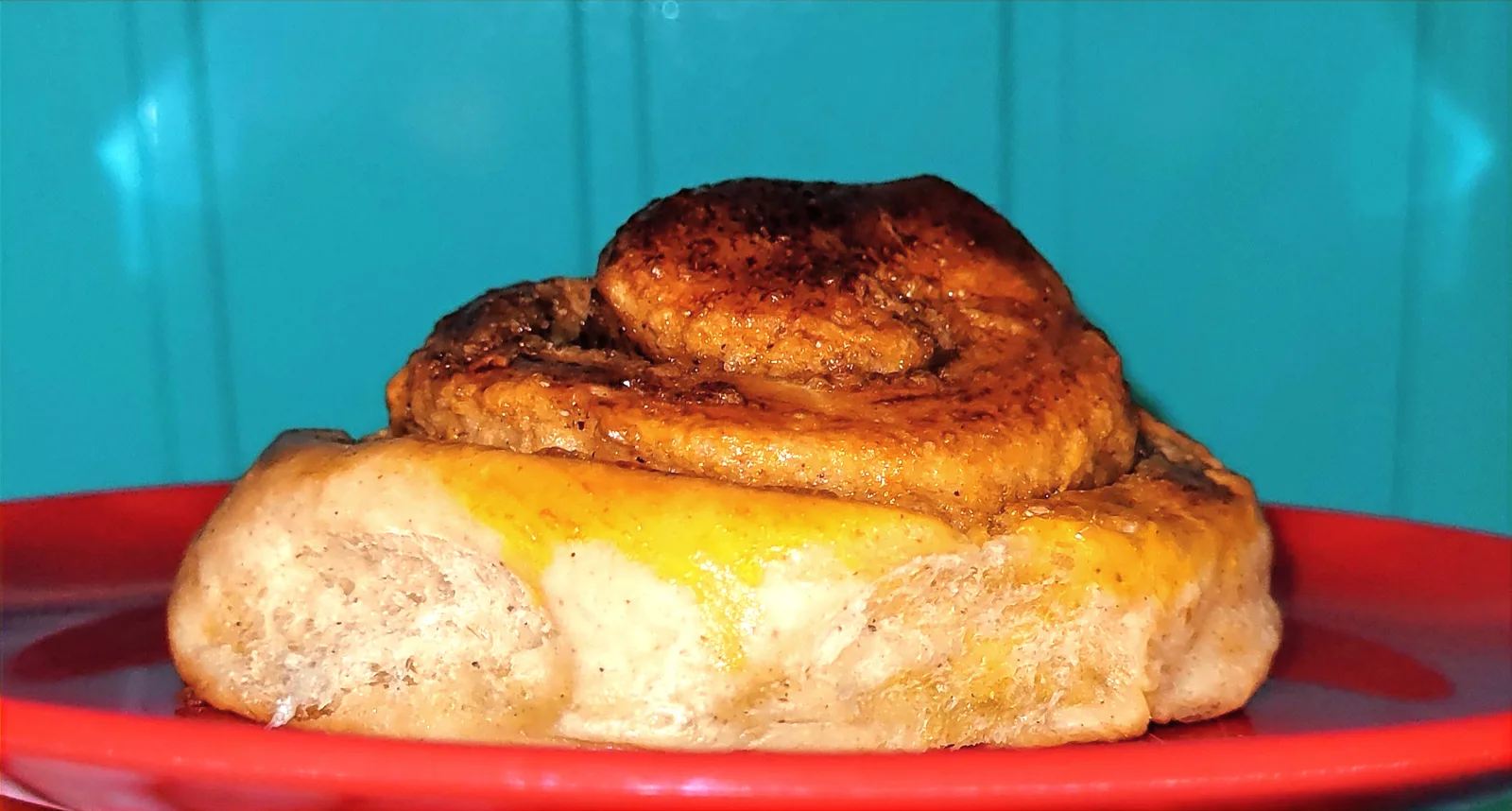 Golden-brown Norwegian cinnamon bun close-up on a red plate with blue wooden background