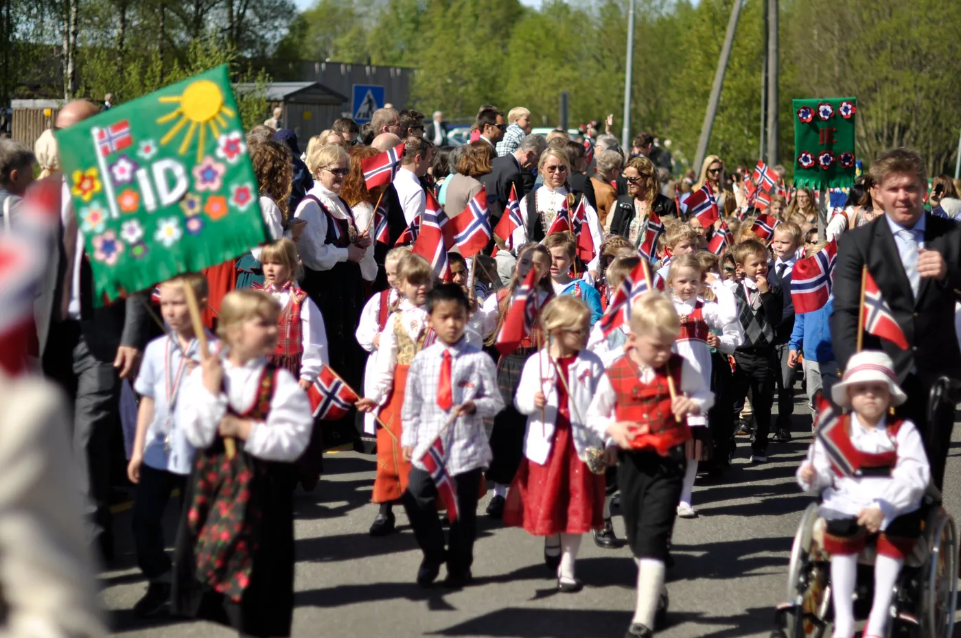 Children in traditional bunad costumes waving Norwegian flags during a modern 17th of May parade