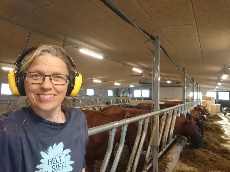 Lise Kaldahl Skreddernes smiling in her barn with cows feeding in the background