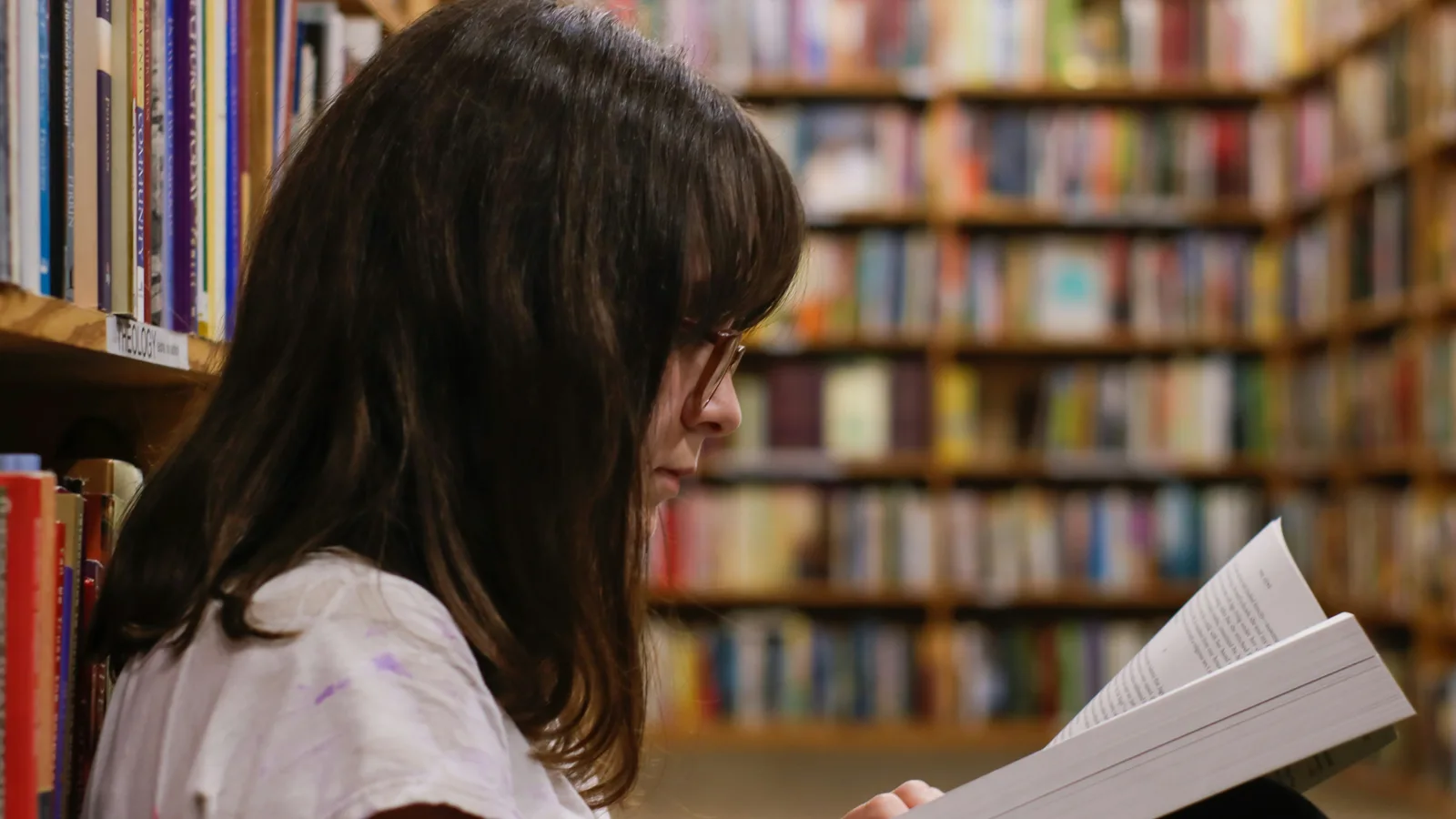 Young woman reading a book in a library surrounded by bookshelves