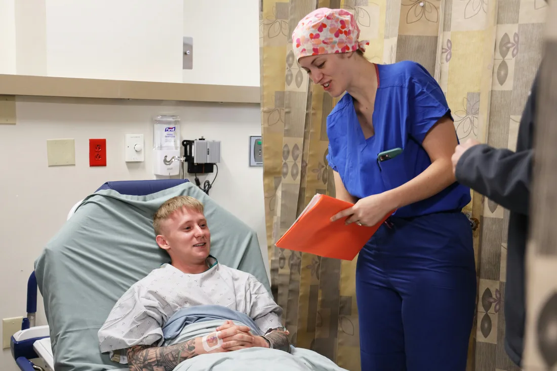 Nurse in blue scrubs reviewing a patient chart at a hospital bedside