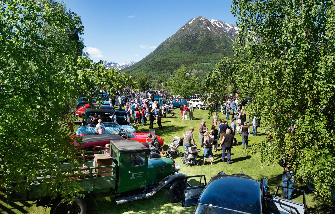 A large crowd of vintage car enthusiasts gathered in Lom, surrounded by classic vehicles and dramatic mountain scenery at the Flåklypa Grand Prix