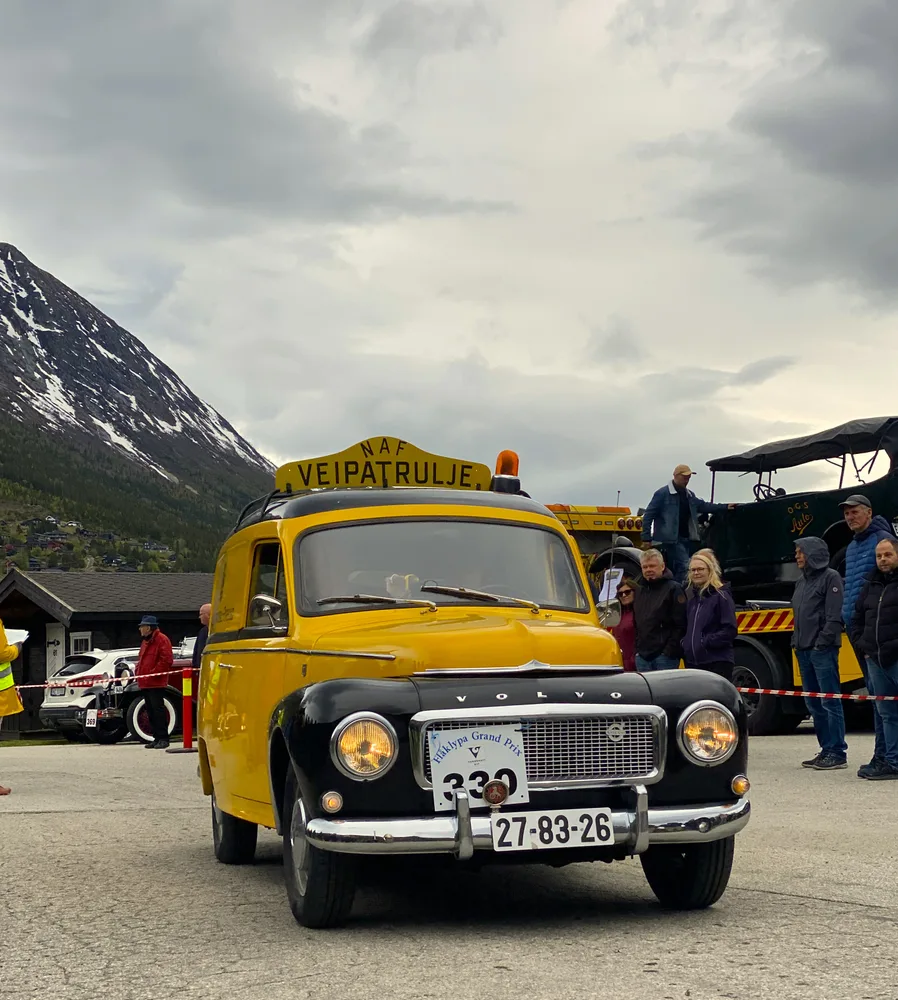 A bright yellow vintage Volvo road patrol car with rally badge at the Flåklypa Grand Prix in Lom, surrounded by spectators and other classic vehicles