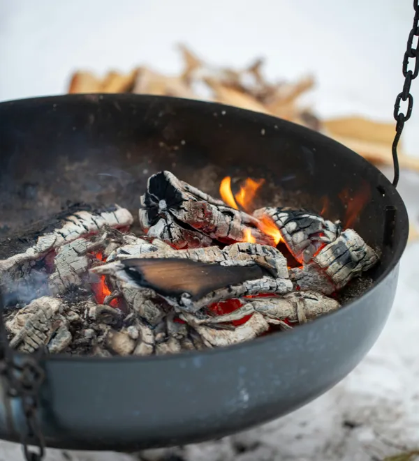 Glowing embers in a hanging fire pit on a snowy winter day
