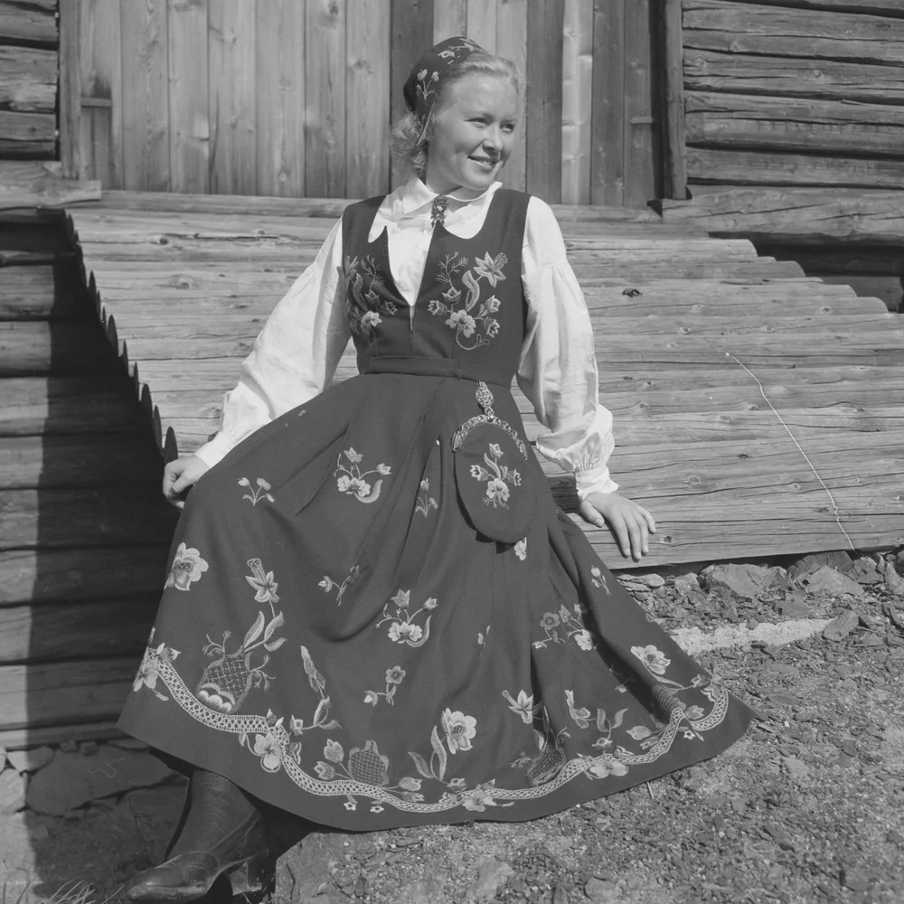A black-and-white photo from 1949 showing a woman seated outdoors wearing a traditional Graffer bunad with a dark bodice and embroidered skirt