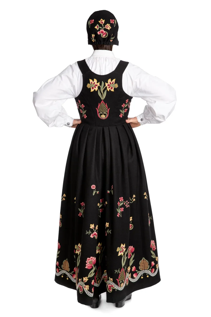 Back view of a woman wearing the black variant of the Graffer bunad, showing detailed floral embroidery on the bodice, skirt, and embroidered headpiece