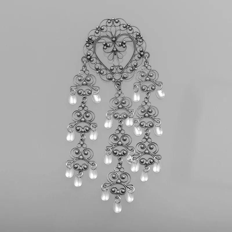 Heart-shaped brooch in traditional filigree silver, featuring delicate scrollwork and multiple dangling filigree drops, worn in Gudbrandsdalen
