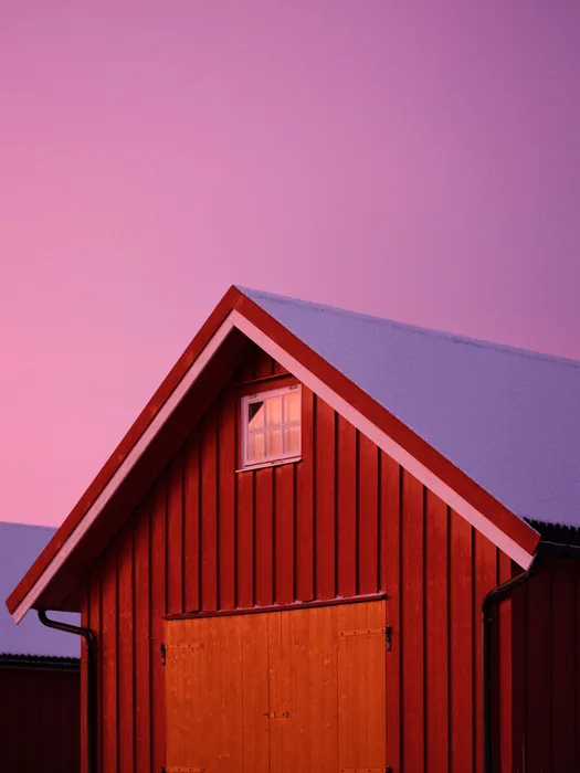 A red boathouse standing at the water's edge under a dramatic purple sky