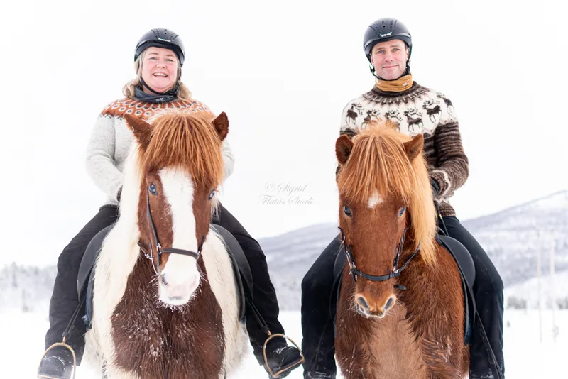 Anne Margrethe and Morten riding Icelandic horses through a snowy winter landscape in traditional Icelandic sweaters
