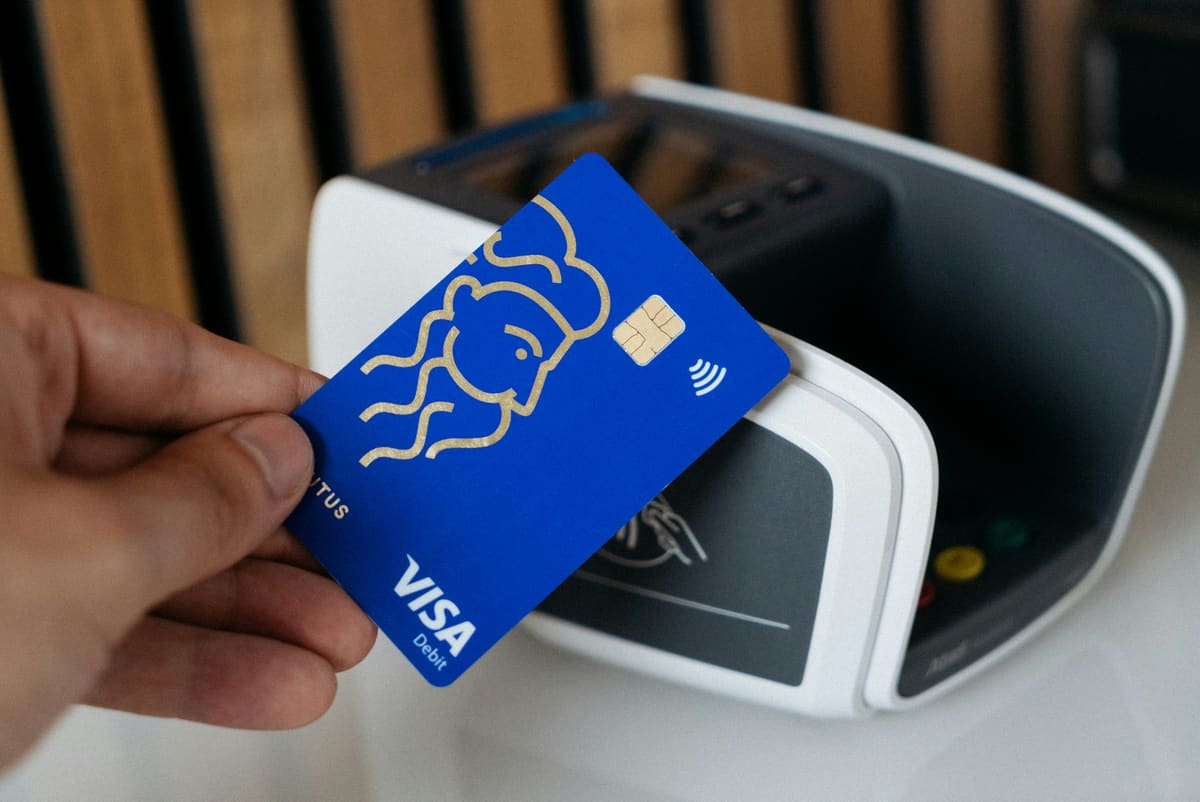 A hand tapping a blue Visa debit card against a contactless payment terminal