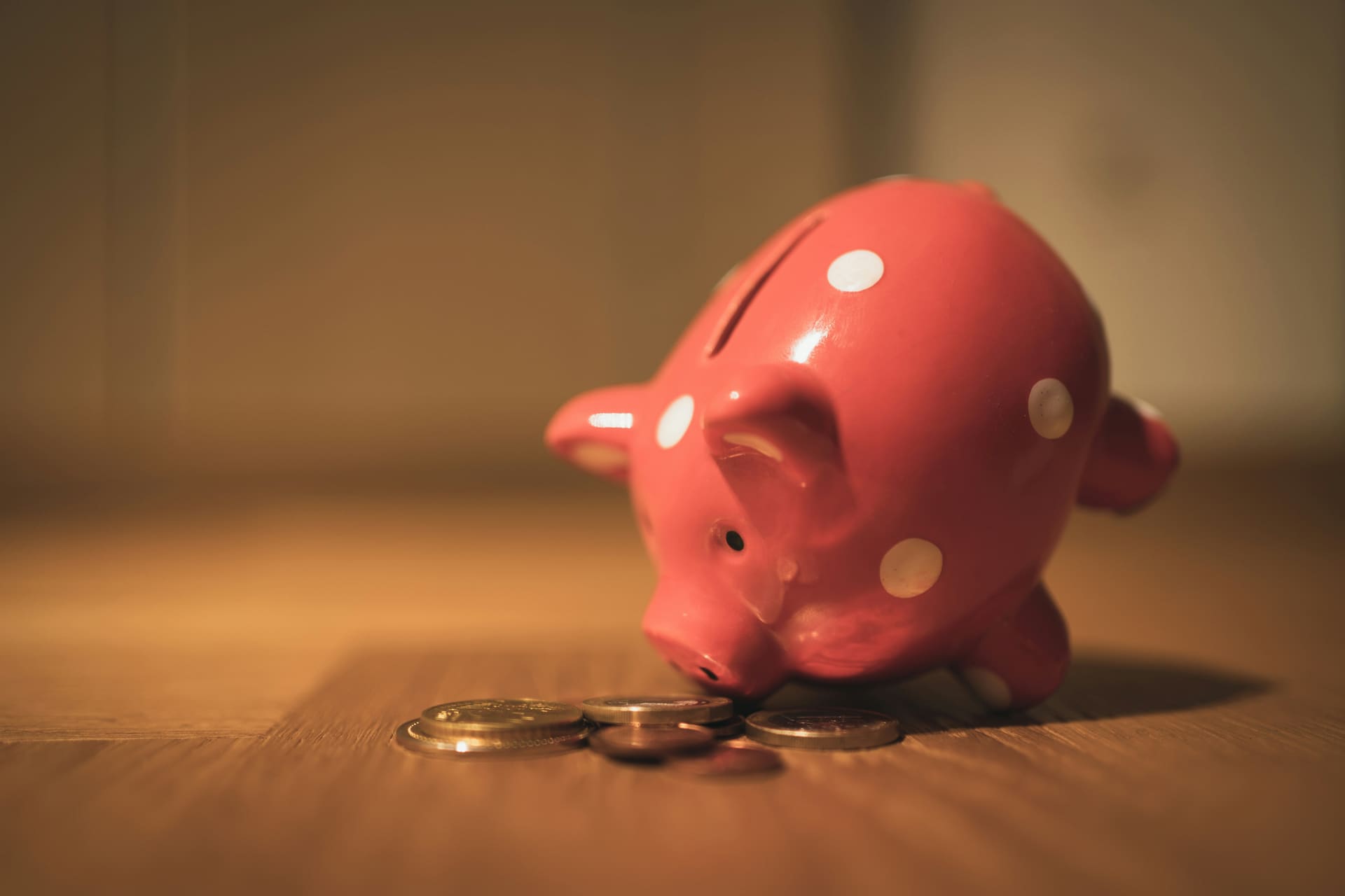 A pink polka-dot piggy bank with coins on a wooden surface in warm light