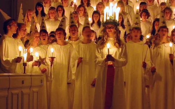 Young woman in white dress wearing a crown of lit candles for Saint Lucia Day