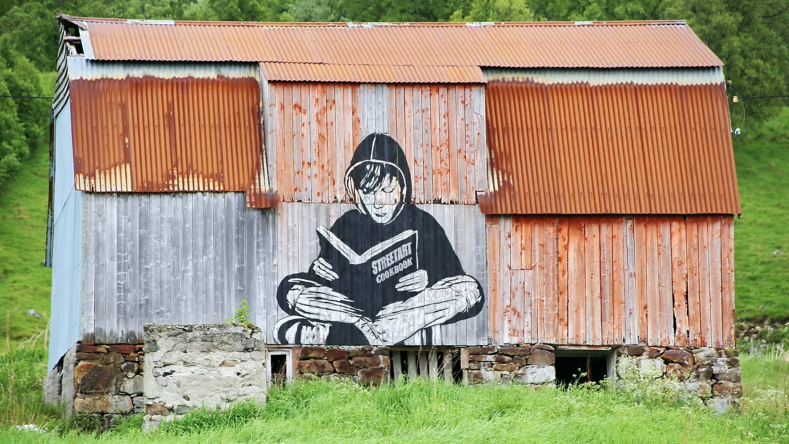 Street art mural of a person reading a book painted on the side of a rustic Norwegian barn