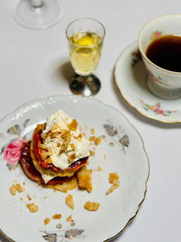 A layered dessert with cream, pastry and seasonal fruit on a floral vintage plate, with coffee and dessert wine