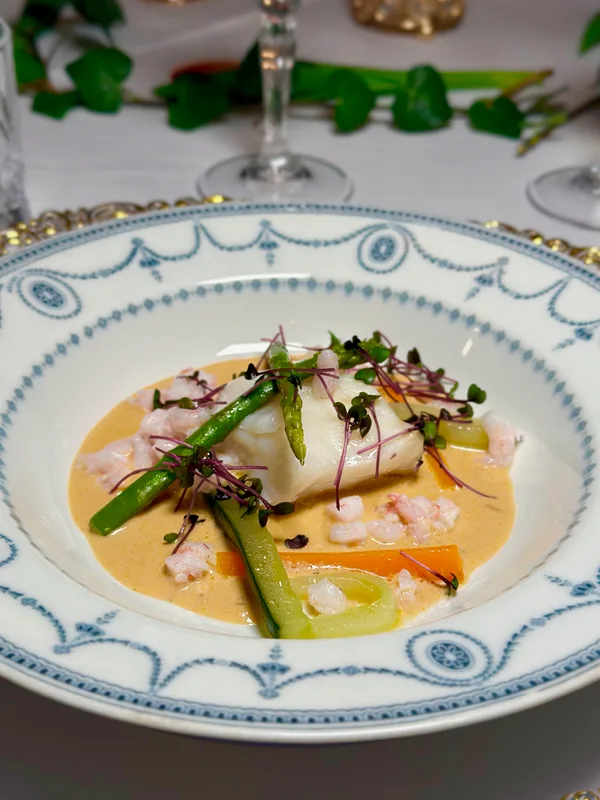 Cod with shrimp, asparagus and microgreens served on a blue-patterned antique plate at Oldemors Hus
