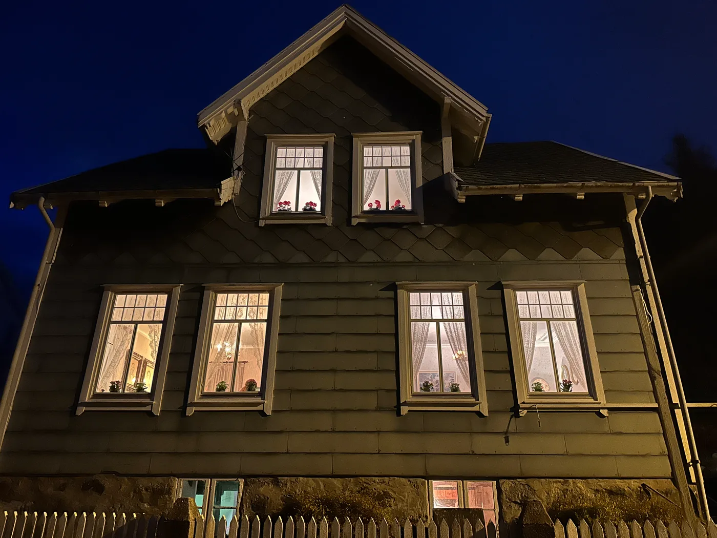 Oldemors Hus from the outside at dusk, a charming wooden house with warm light glowing from every window