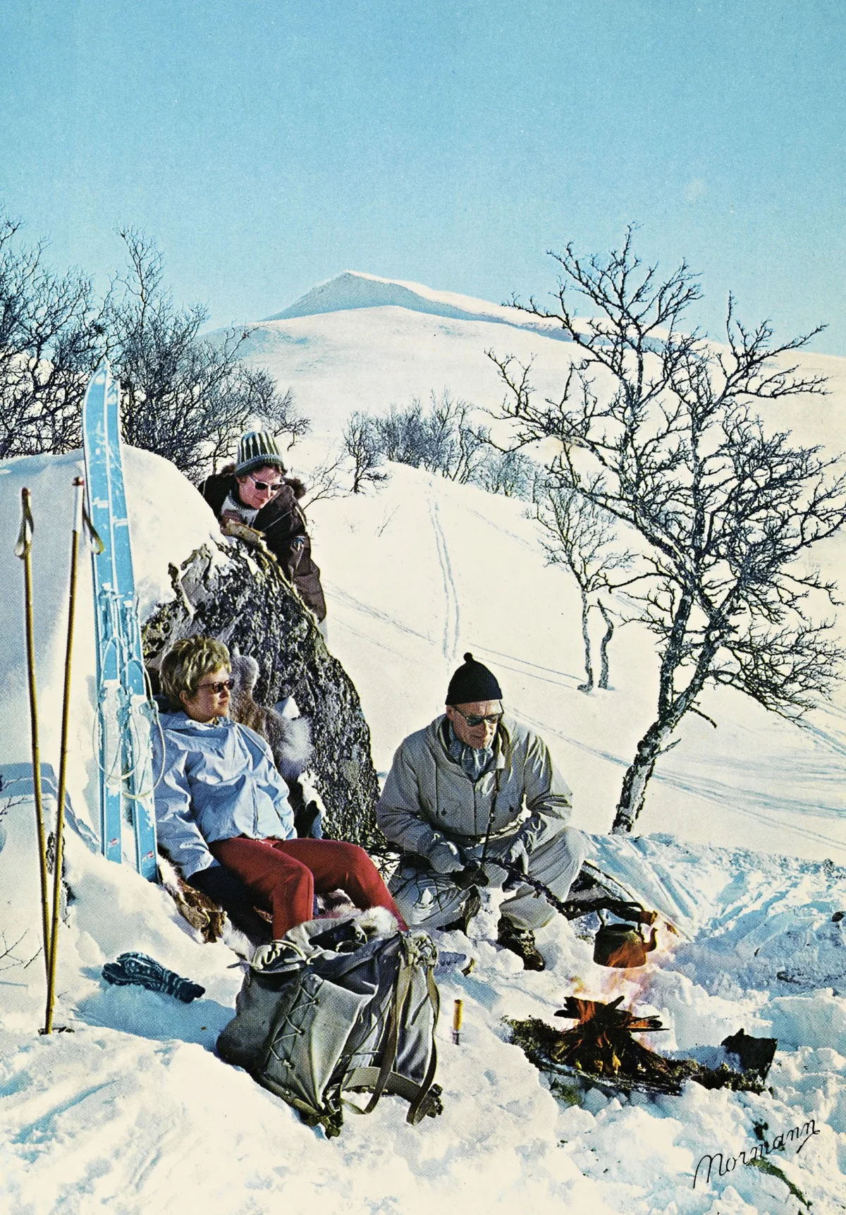 Classic Norwegian Easter scene on a sunny mountain plateau with three people gathered around a campfire beside their skis and backpacks