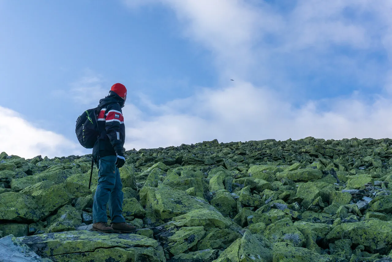 A hiker near the summit of the mountain Muen in Rondane, looking out over a vast mountain landscape under a blue sky