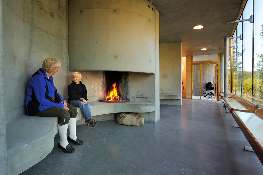 A cozy timber cabin at Strømbu Rest Area with warm lighting, surrounded by birch trees in autumn on the Rondanevegen route