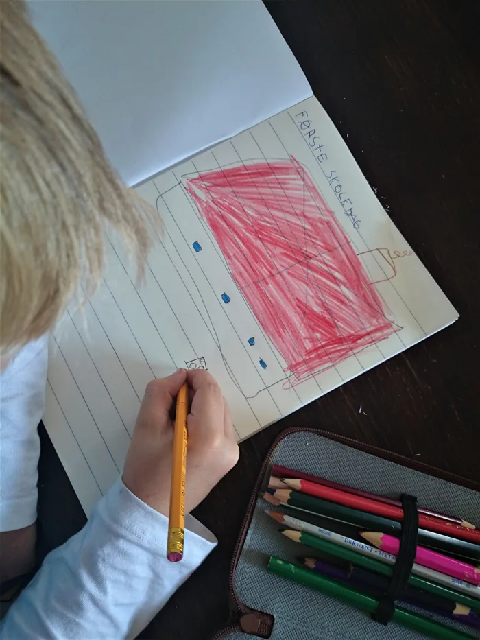A young boy writing and drawing in a workbook on his first day at school