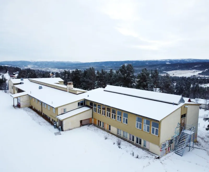 Aerial drone photo of the current Verket School building in Folldal, covered in snow with mountains in the background