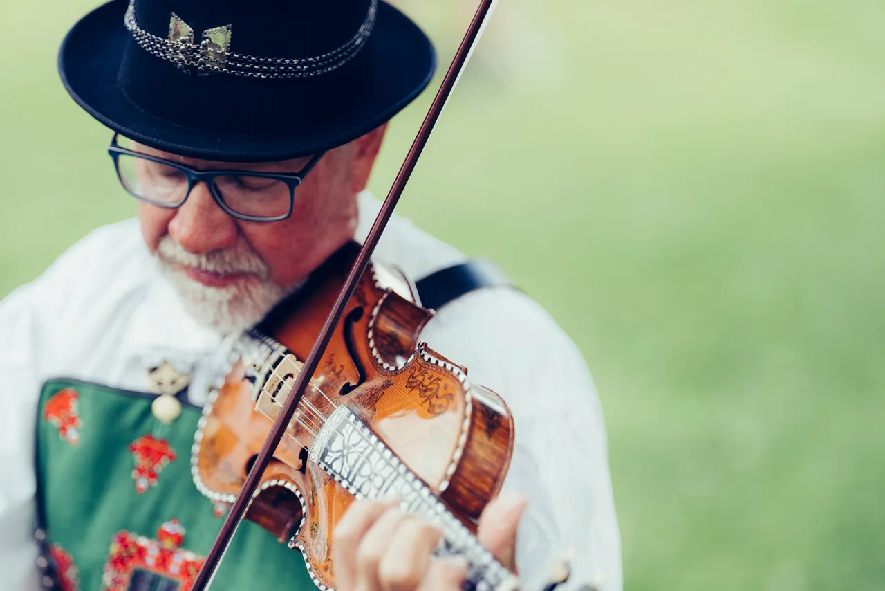 A man in traditional Setesdal bunad playing the Hardanger fiddle outdoors