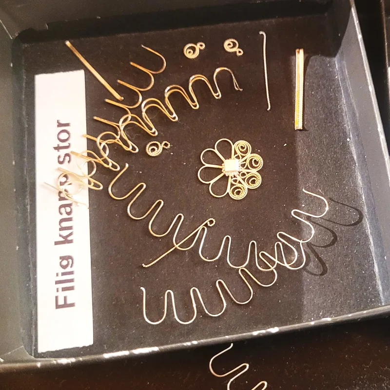 A tray labelled ‘Filig knappstor’ showing various filigree wire shapes and a completed silver flower element