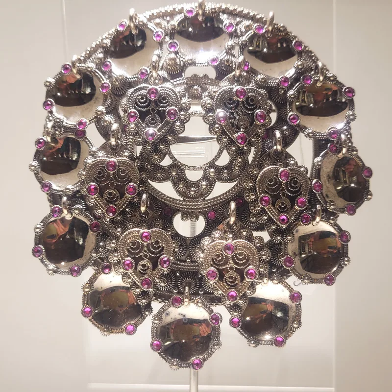 A large silver sølje brooch with filigree hearts, hanging mirror-like discs, and purple gemstones set throughout