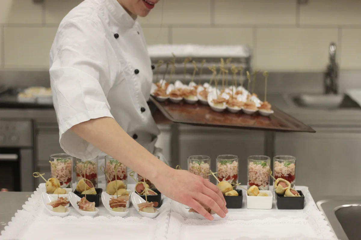 A chef in professional whites carefully arranging canapés on a platter in a commercial kitchen