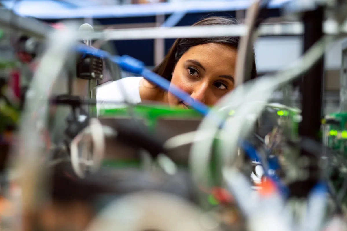 A young woman focused on technical engineering work, peering through electronic equipment