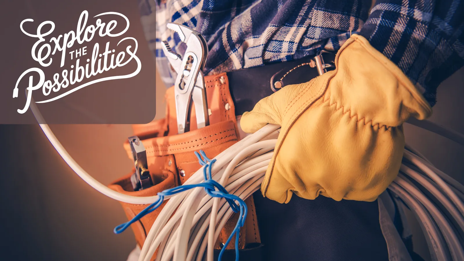 A skilled worker wearing a tool belt and holding electrical cables, with the text 'Explore the Possibilities'