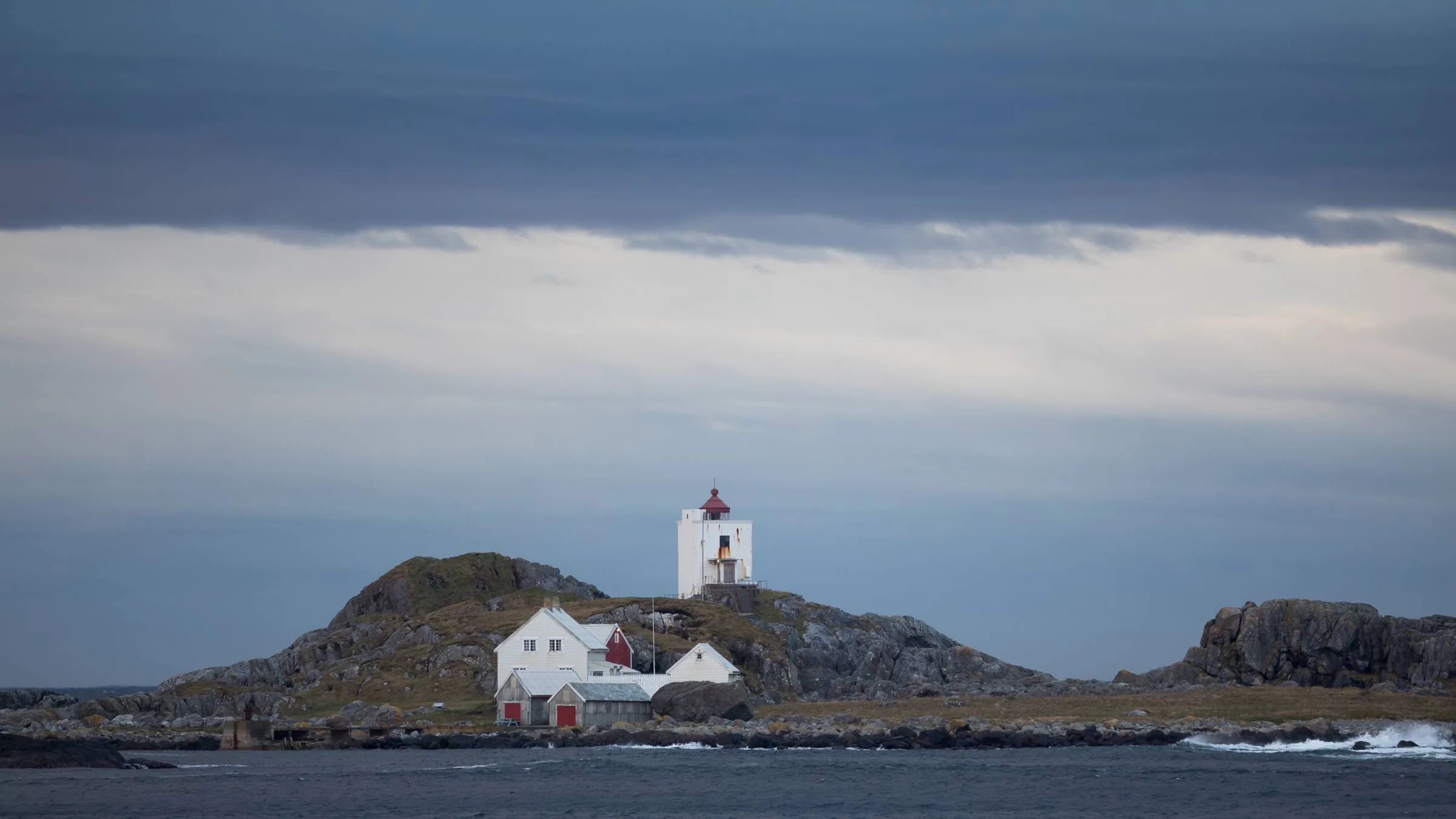 Ulla Lighthouse on Kvernholmen under dramatic dark storm clouds with surrounding buildings and the sea