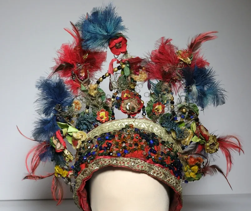 A reisle bridal headpiece from 1855, on display at the Vest-Agder Museum, made of wool fabric, silver lace, colourful glass beads, fabric flowers, feathers, and silver