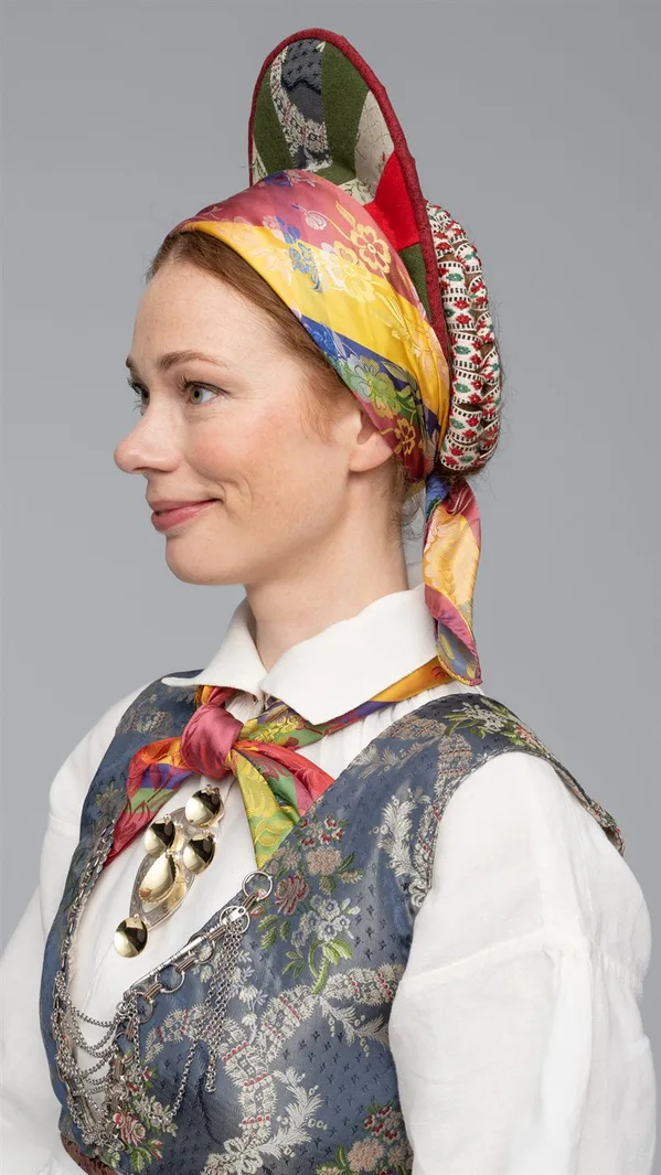 A decorated vase headpiece for the Vest-Agder bunad, richly adorned with applied fabrics, ribbons, and metal ornaments