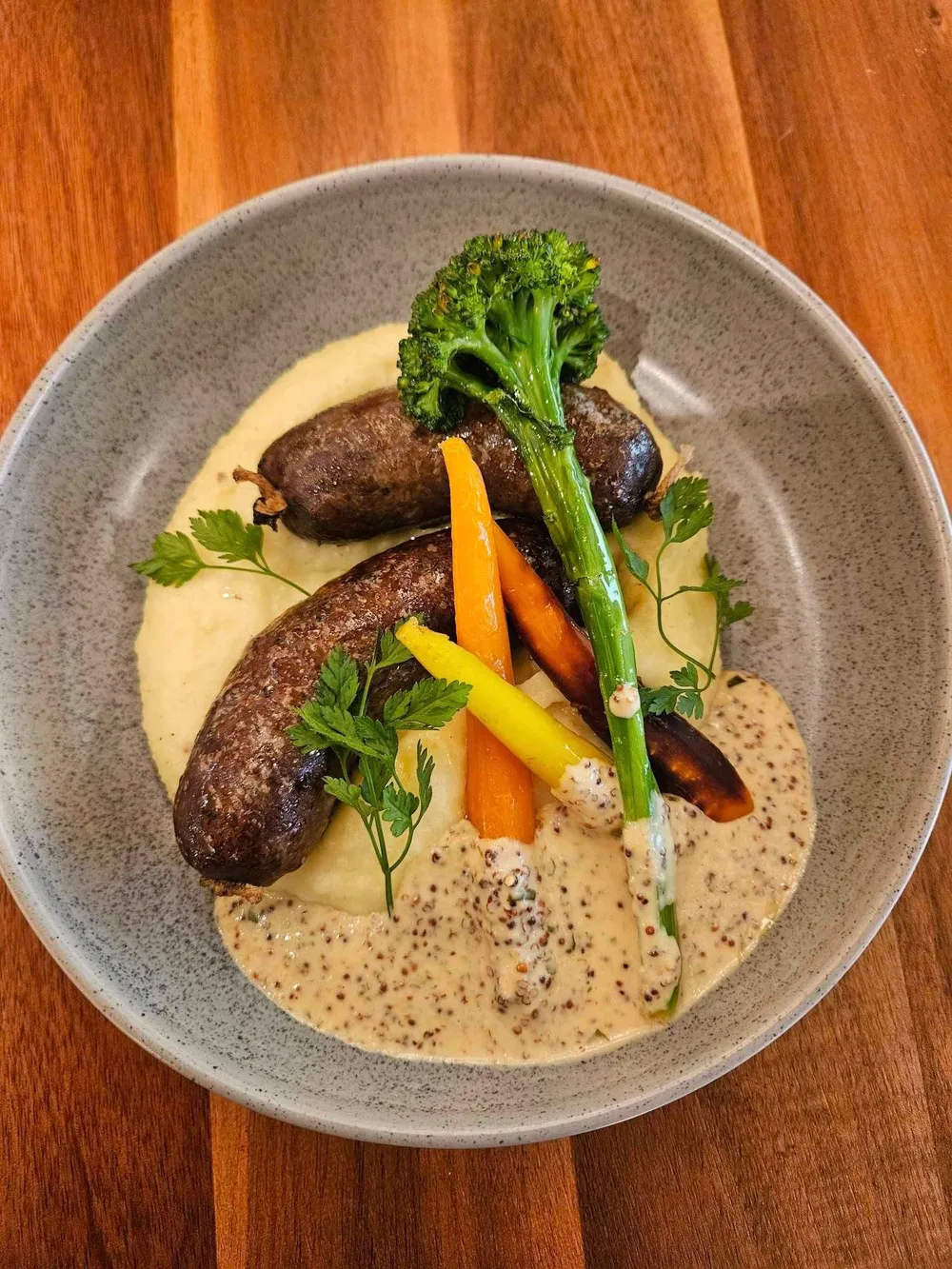 A gourmet plate of wool pig sausages served with roasted root vegetables, broccolini, and mustard cream sauce