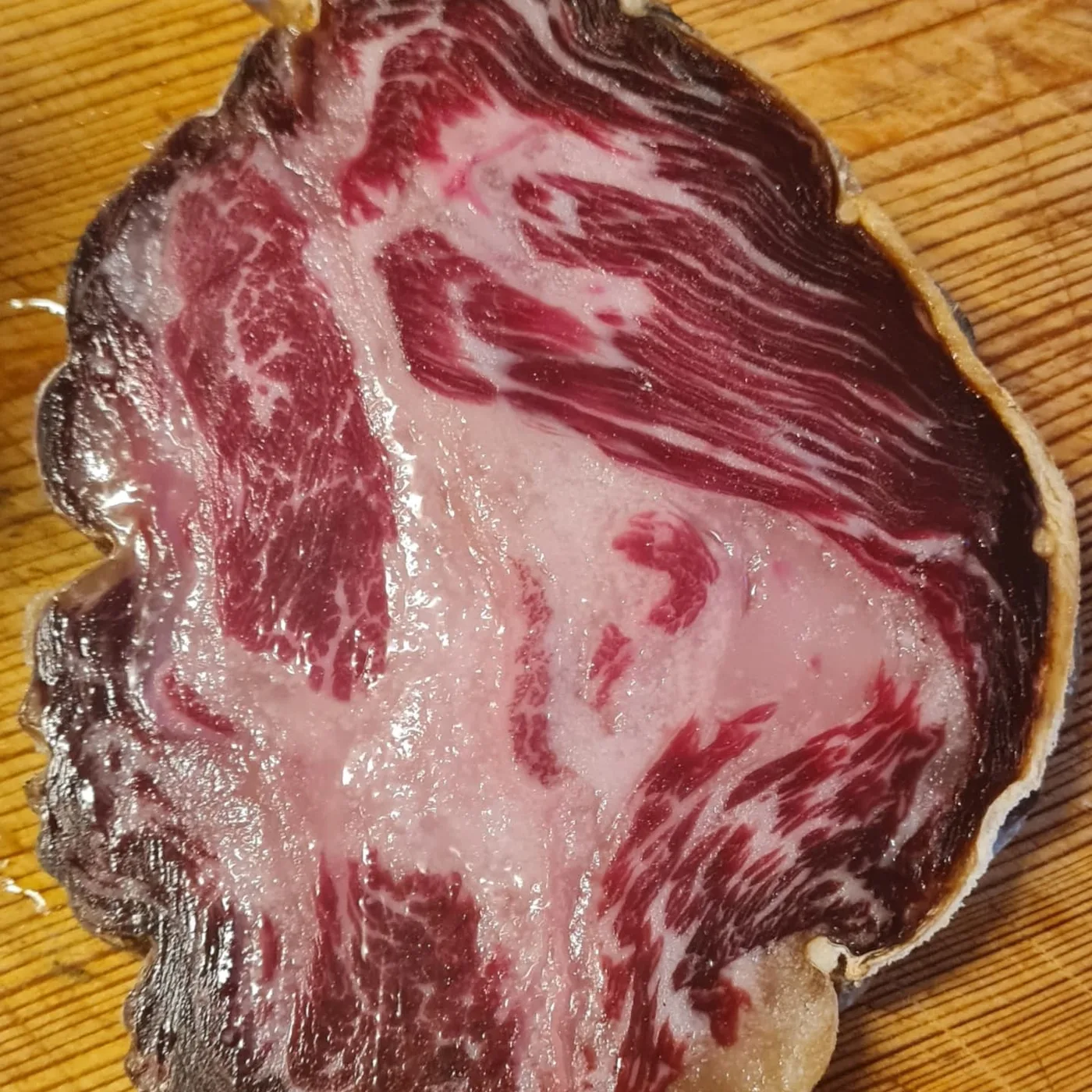 Slices of dark, richly colored cured wool pig meat arranged on a rustic wooden surface