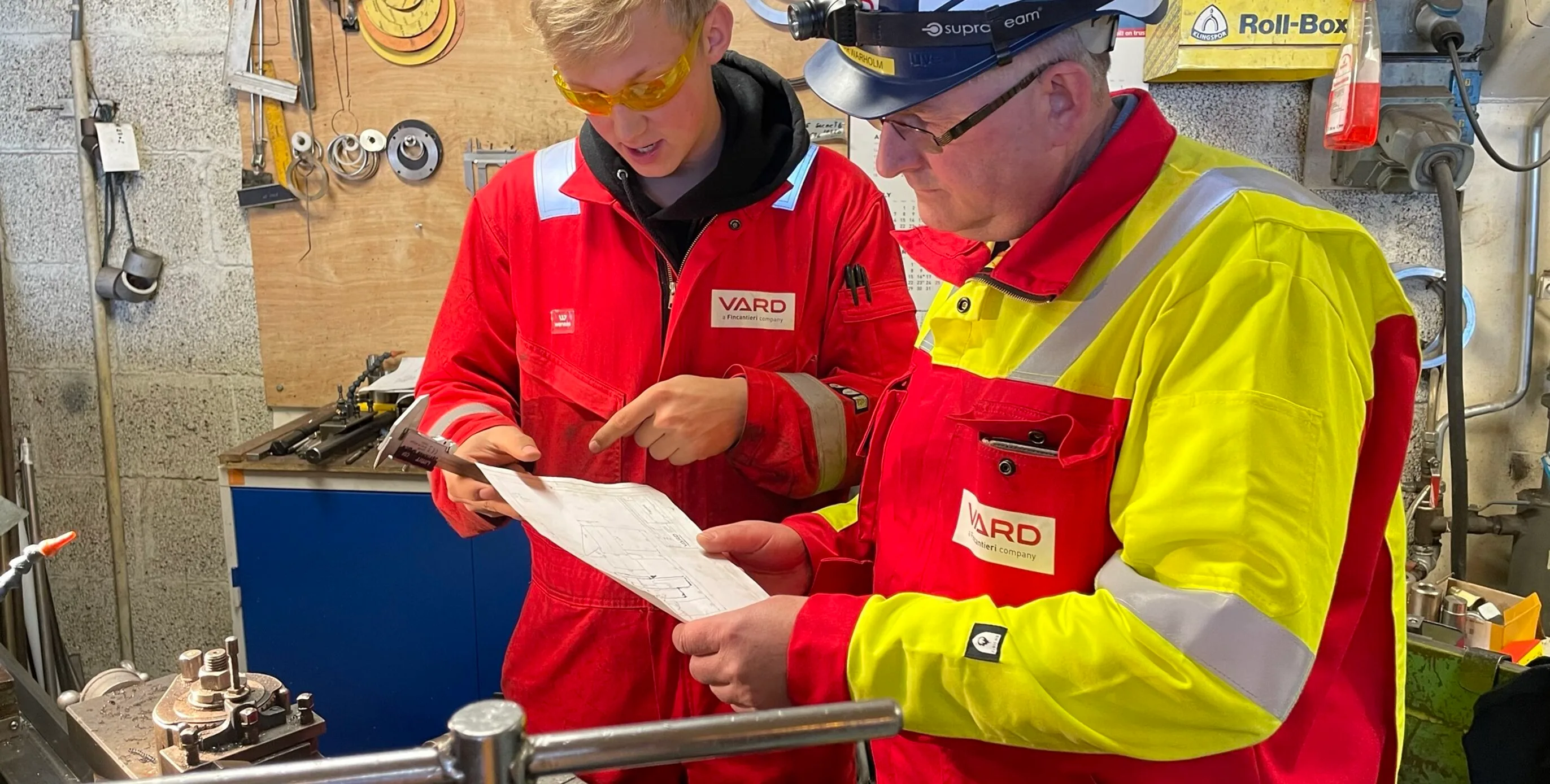 Two VARD workers in protective clothing study a work sheet together in the workshop, reflecting the close teamwork Odd-Einar describes.