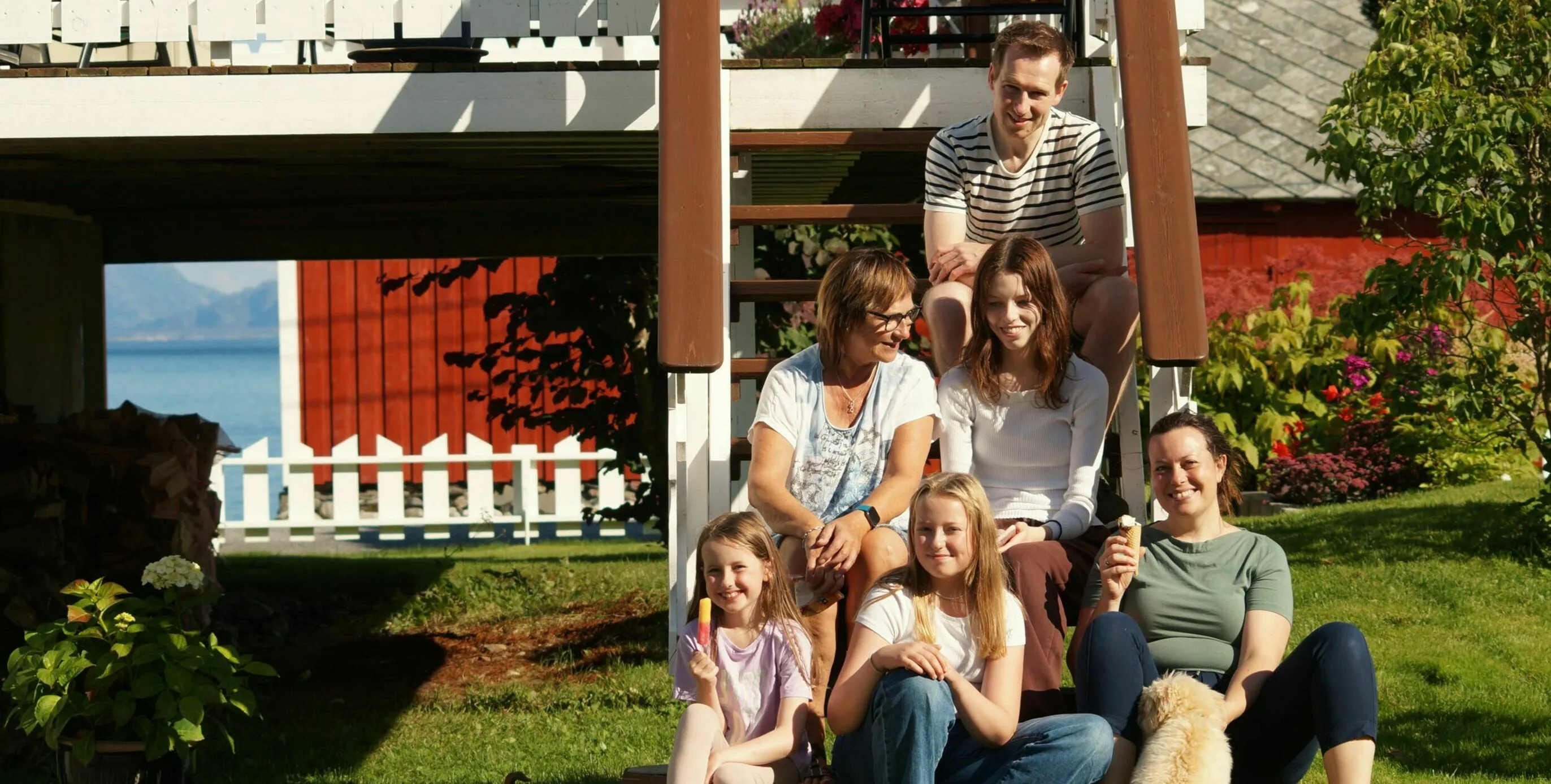 Arnt Inge with family and friends sitting on steps outside a red house in Eidsvika, with the sea visible in the background.
