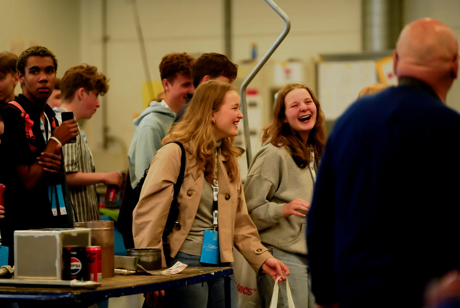 Smiling teenagers and a VARD guide talking together in a workshop area during the Student Evening, with students in casual clothes and safety gear gathered around activity stations.