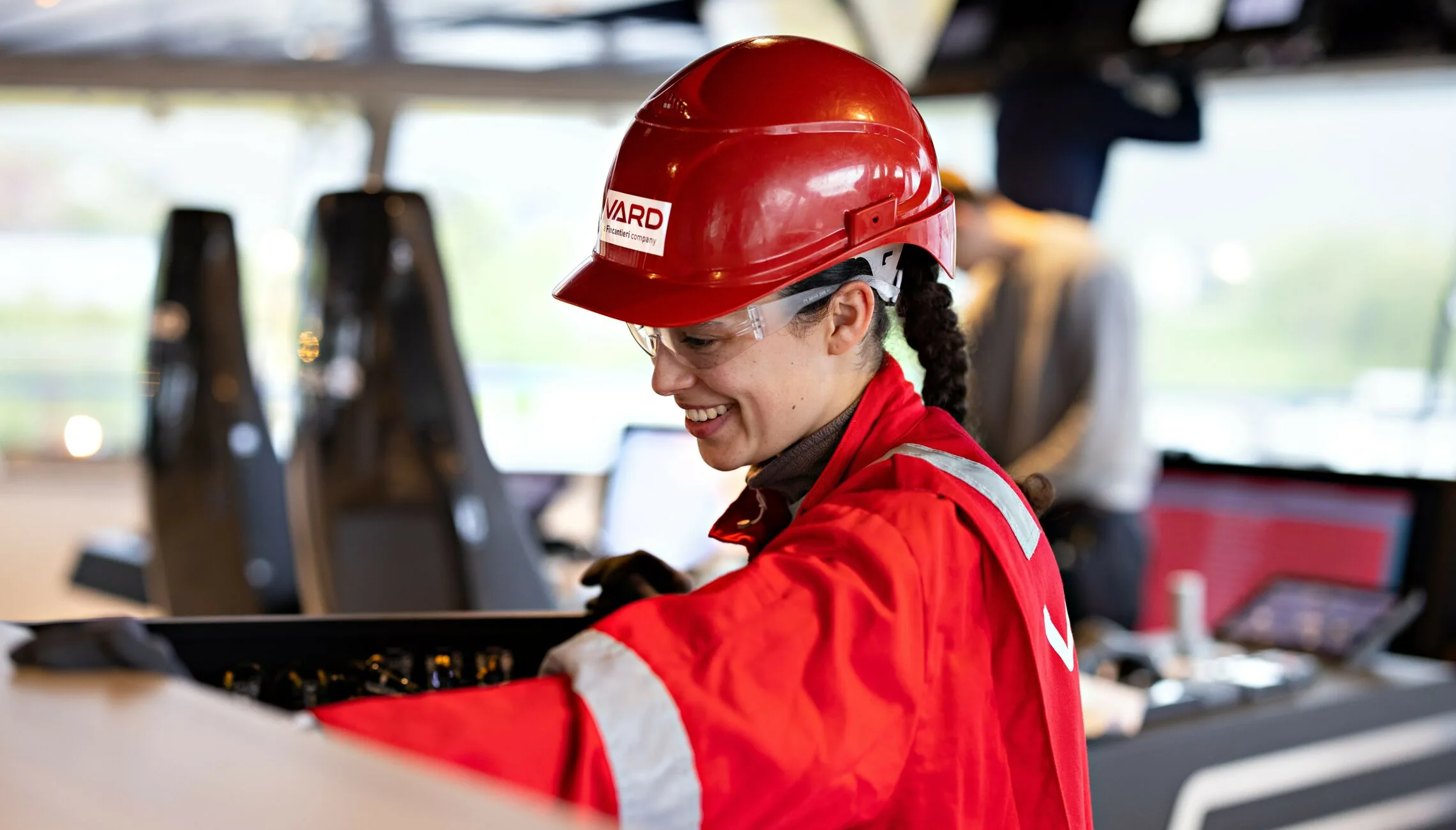 Smiling VARD employee in red coveralls and a hard hat working onboard a vessel.