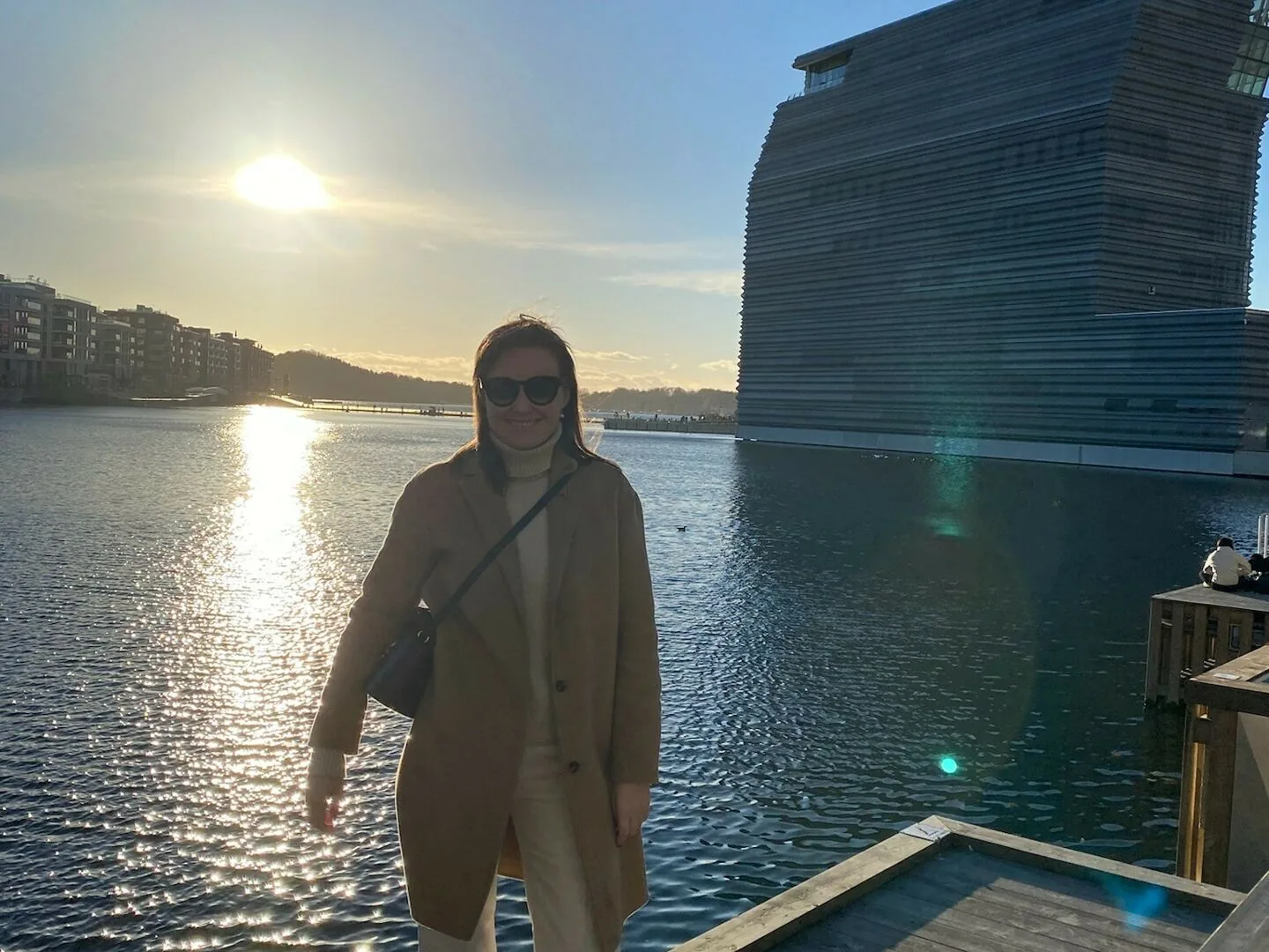 Woman standing on a dock by the Oslo waterfront with the sun reflecting on the water.
