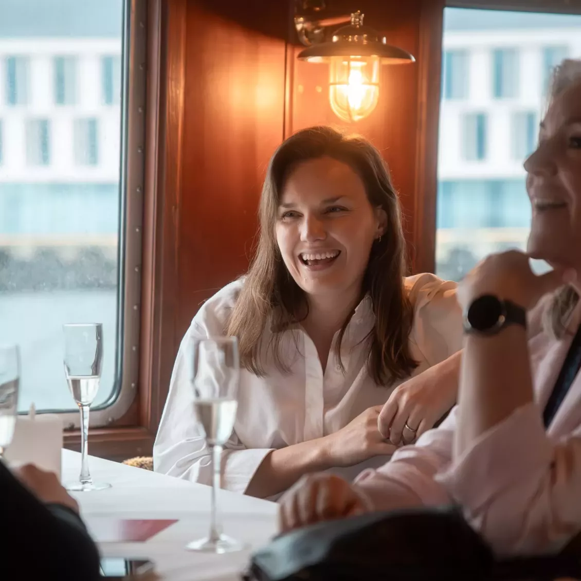 Woman smiling and chatting at a café table with friends, with drinks on the table.