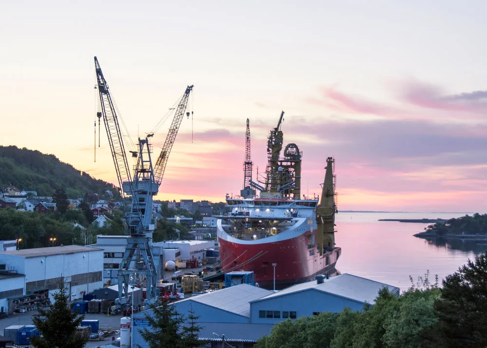 Industrial harbor in Brattvåg with a large red offshore vessel and tall cranes at sunset