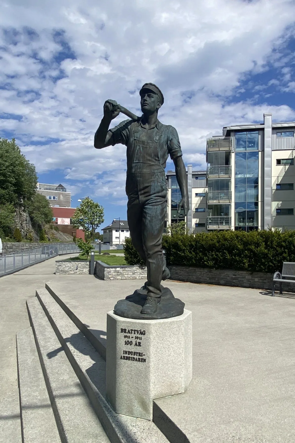 Bronze statue of an industrial worker on a pedestal in Brattvåg, with modern buildings behind