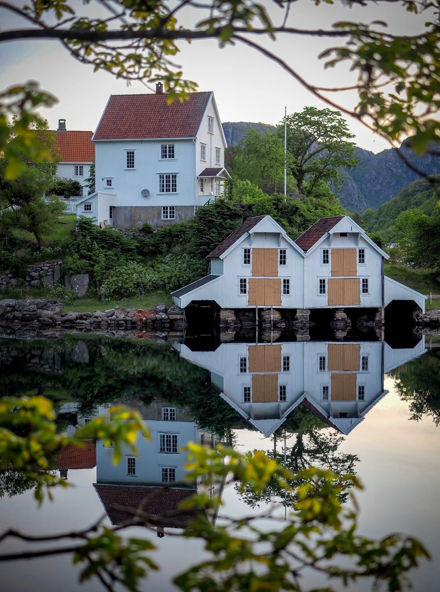 A charming house and two boat houses reflected in still water at Hidra